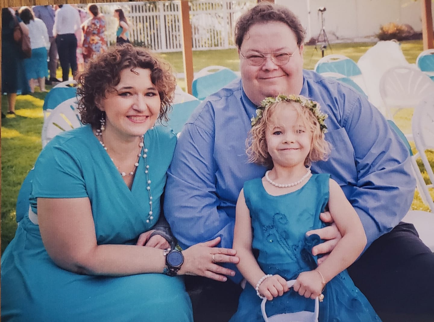 Smiling family in teal outfits, consisting of a man, woman, and a little girl wearing a teal dress