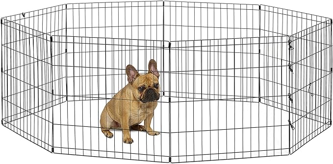 A French Bulldog puppy sits inside a metal cage, known as a Puppy Exercise Pen.